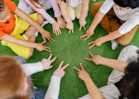 Children sitting in a circle playing fun team games on artificial grass.
